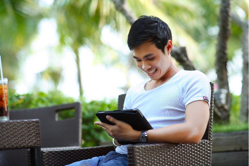 Man sitting on an outdoor table, looking at a tablet
