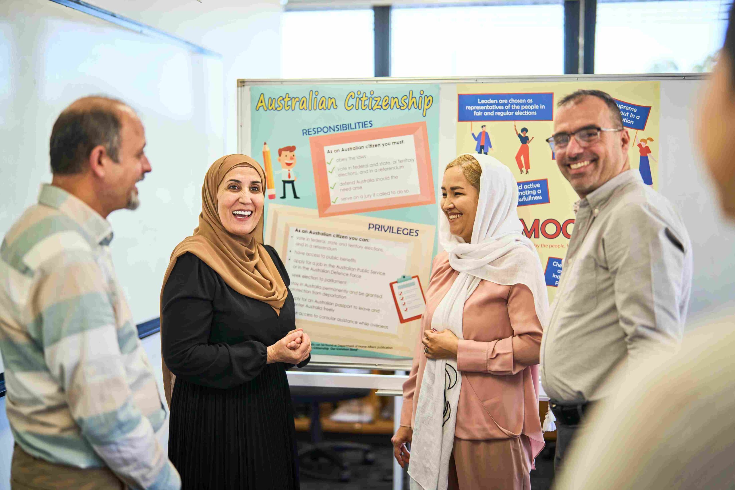 Four students standing in front of a noticeboard reading Australian citizenship key facts in a classroom