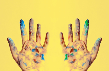 Two hands with palms facing upward, covered in colourful paint